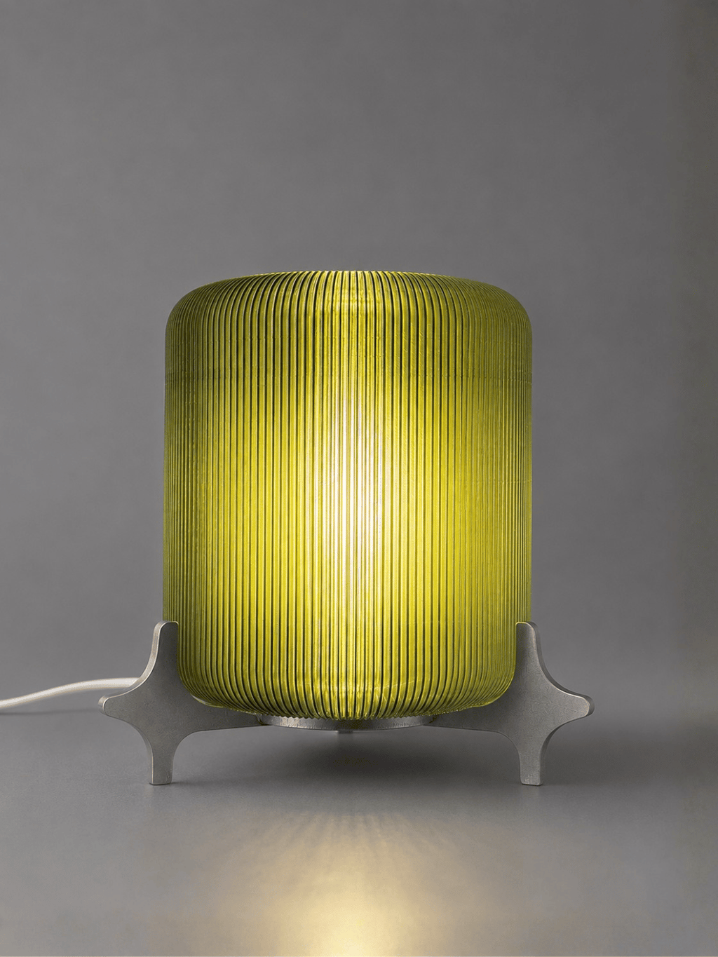 AERO illuminated designer table lamp by Natalia Design Co. featuring a glowing olive green ribbed translucent PETG diffuser and sculptural satin aluminium base for ambient lighting.
