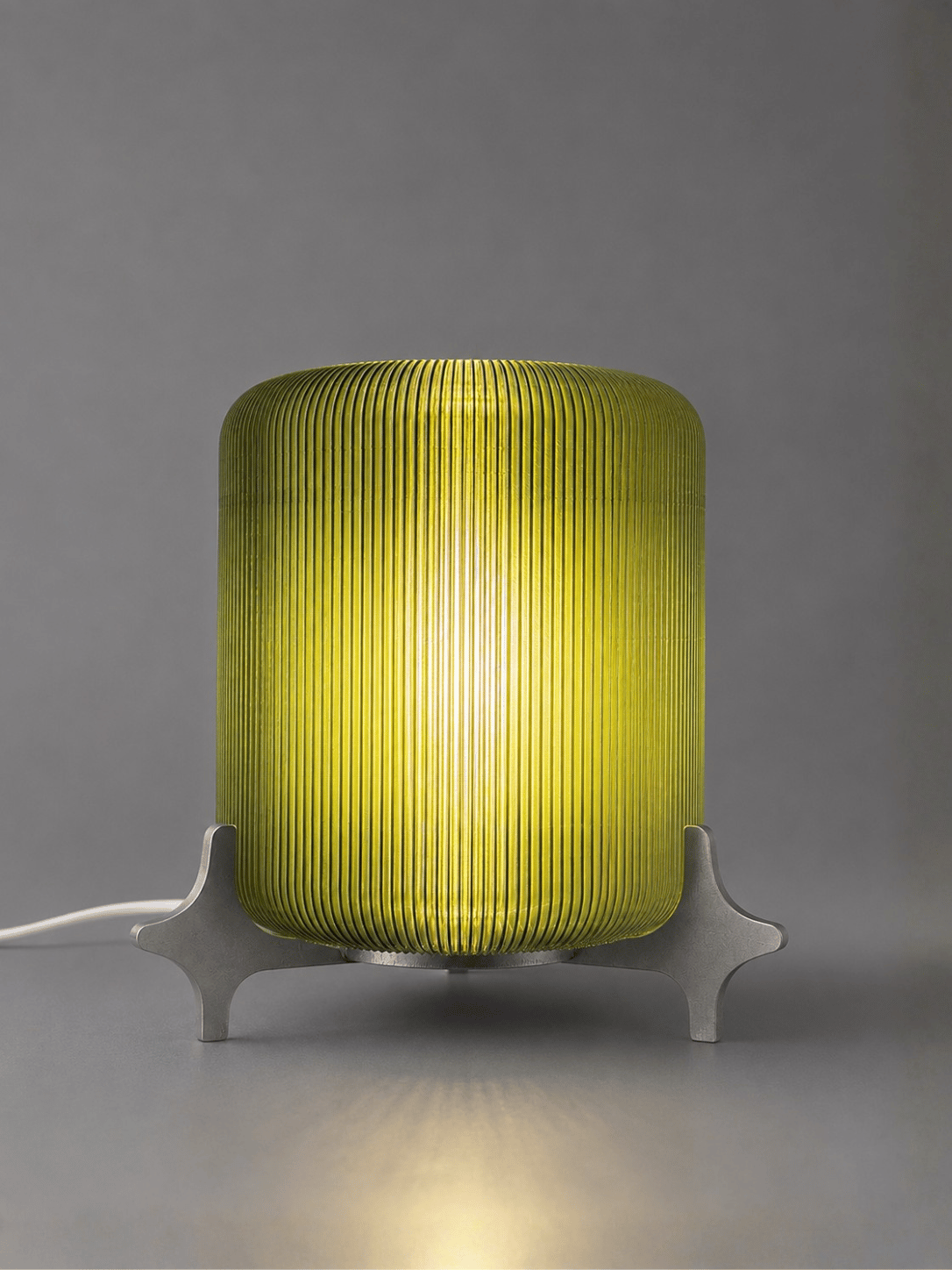 AERO illuminated designer table lamp by Natalia Design Co. featuring a glowing olive green ribbed translucent PETG diffuser and sculptural satin aluminium base for ambient lighting.